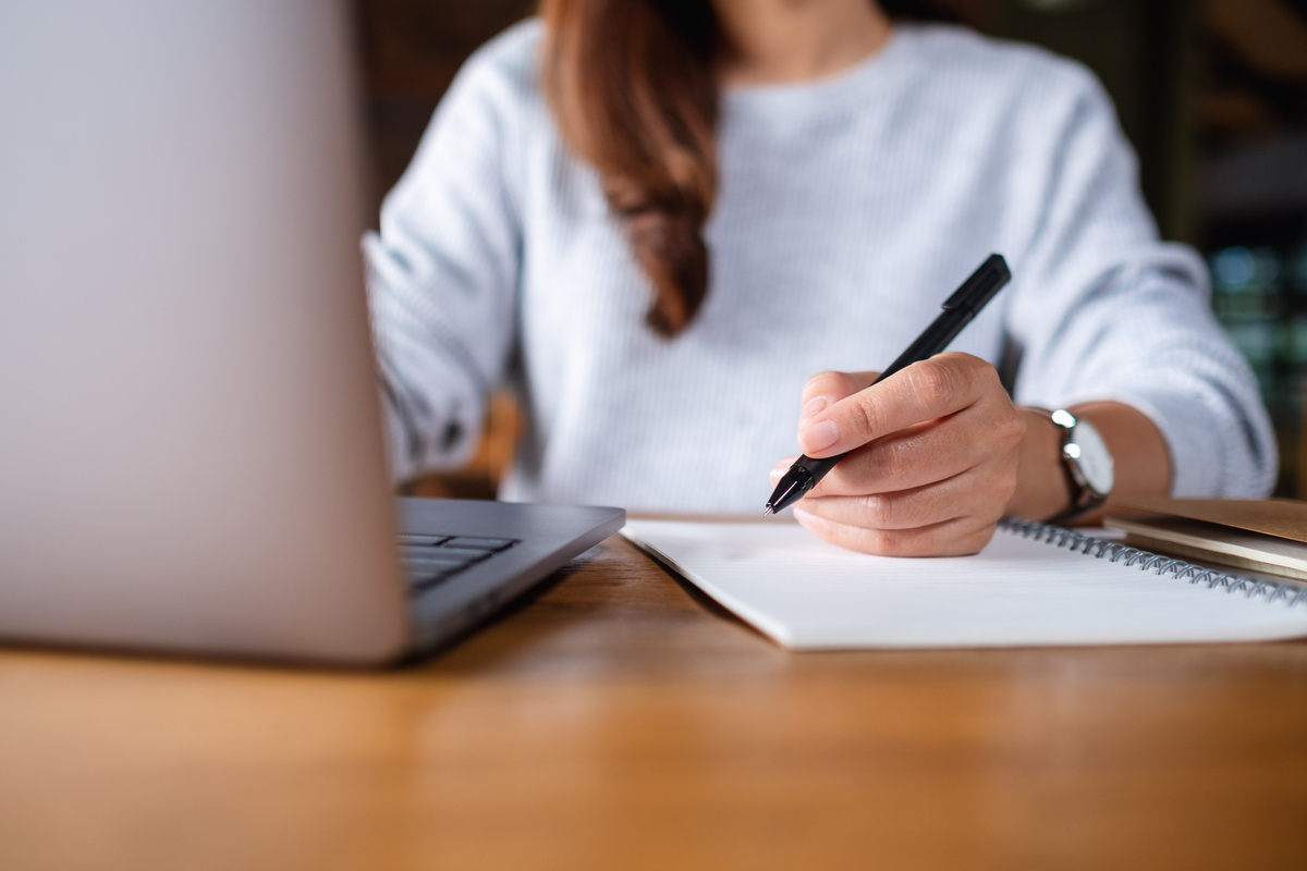 Closeup Image of a Woman Writing on a Notebook While Working on